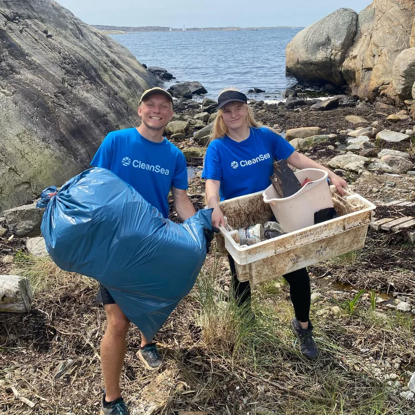 34dce50cecff4413922ab2812e267fb0 Greencarrier News Stories Greencarrier Two volunteers in blue CleanSea shirts collect litter on a rocky shoreline holding a large blue trash bag and a tub of debris