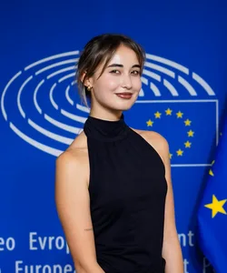 Julieta Martínez standing in front of a blue wall with the european flag behind She is smiling to the camera